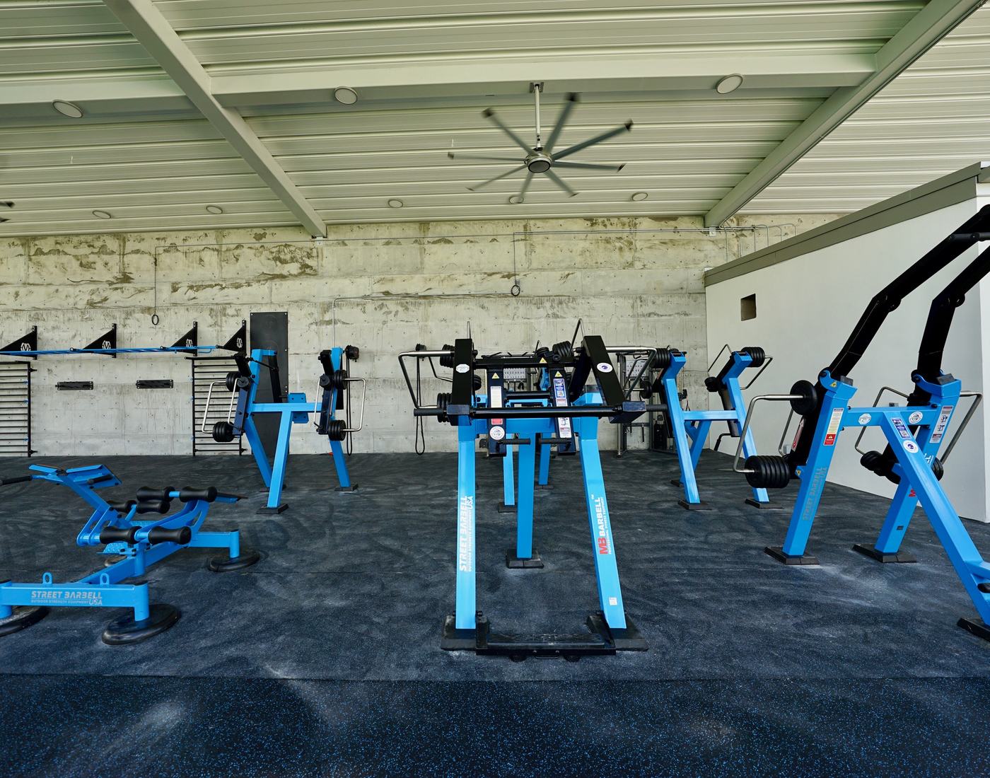 Blue StreetBarbell plate-loaded machines in a covered outdoor gym